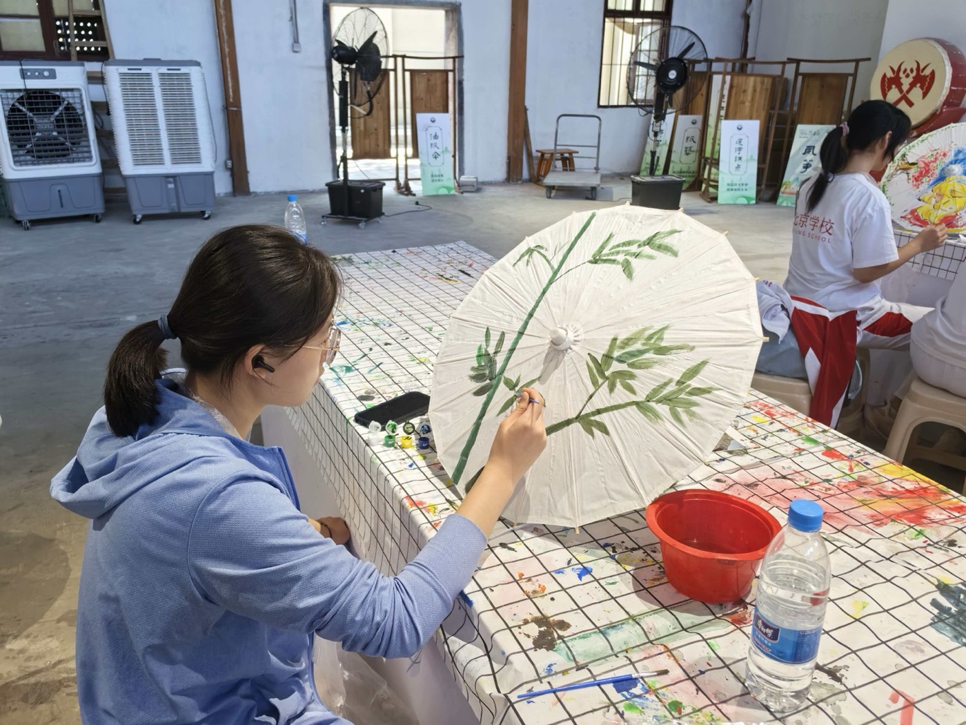 A visitor hand-painting bamboo leaves onto a white oil-paper umbrella