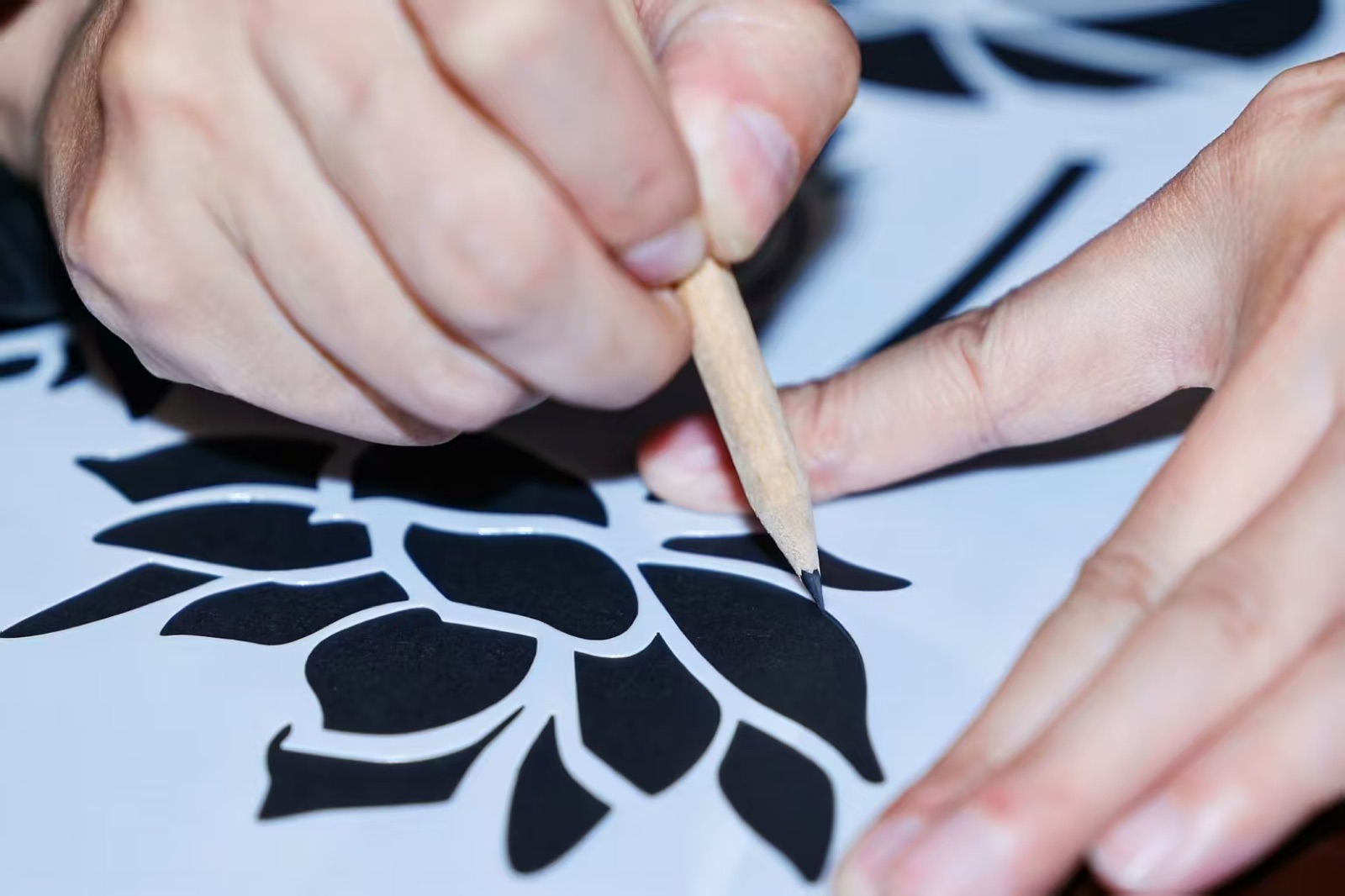 Hands cutting an intricate black floral paper-cut design with a knife