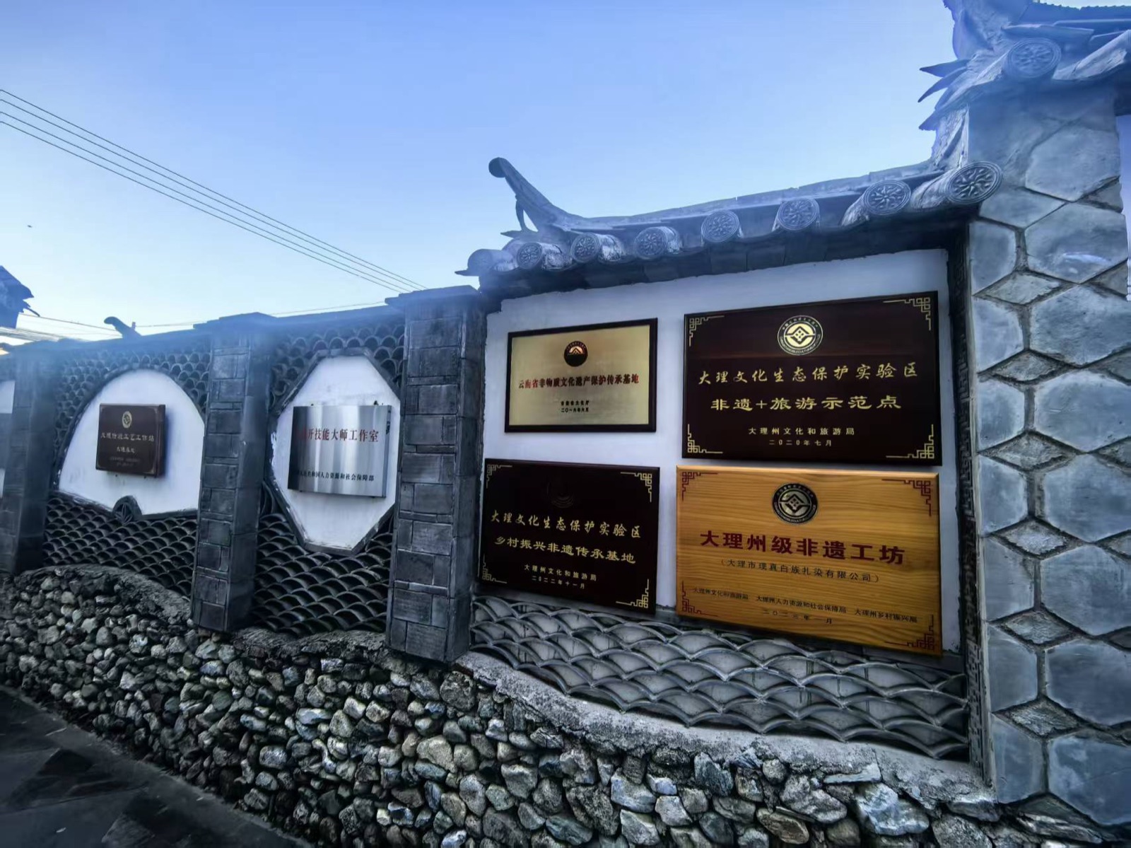 Heritage plaques on a Zhoucheng workshop wall naming it a Yunnan intangible-heritage base